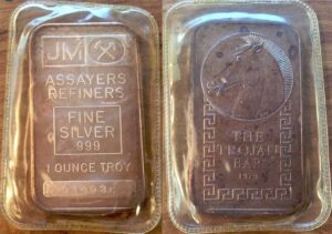 Front and back of Johnson Matthey 1 oz silver "The Trojan Bar". Front stamped JM Fine silver 999 with serial number. Back depicts Trojan horse with border, stamped "The Trojan Bar 1979".